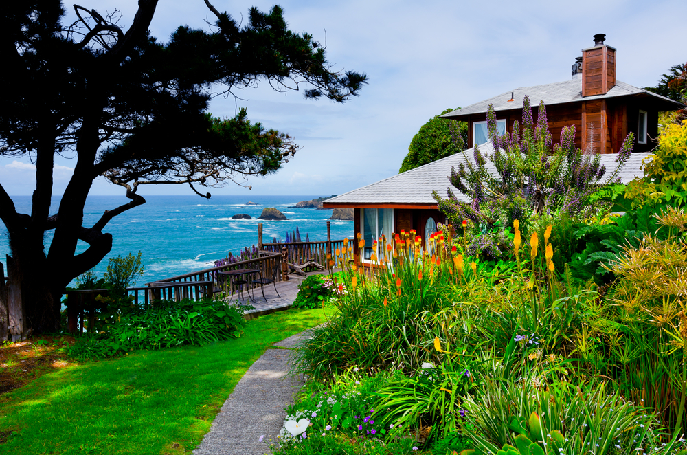 Oceanside home with large garden in front of it and well kept lawn.