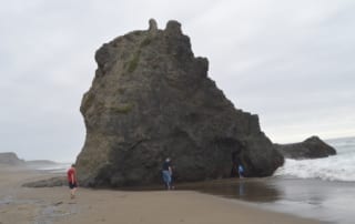 Three people walking on California beach looking at large lone rock outcrop.