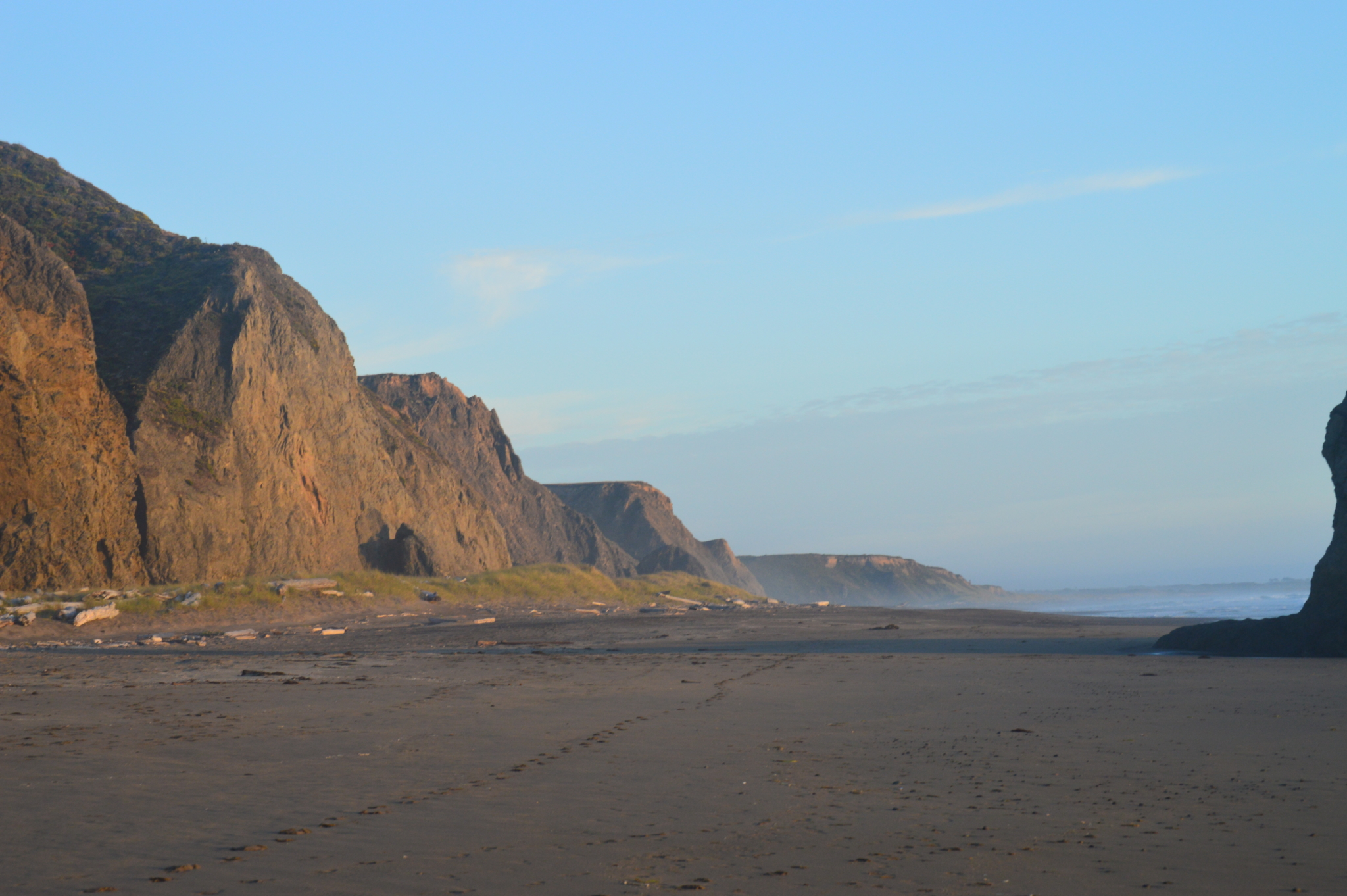 Oceanside cliffs leading to a beach with footprints at sunset