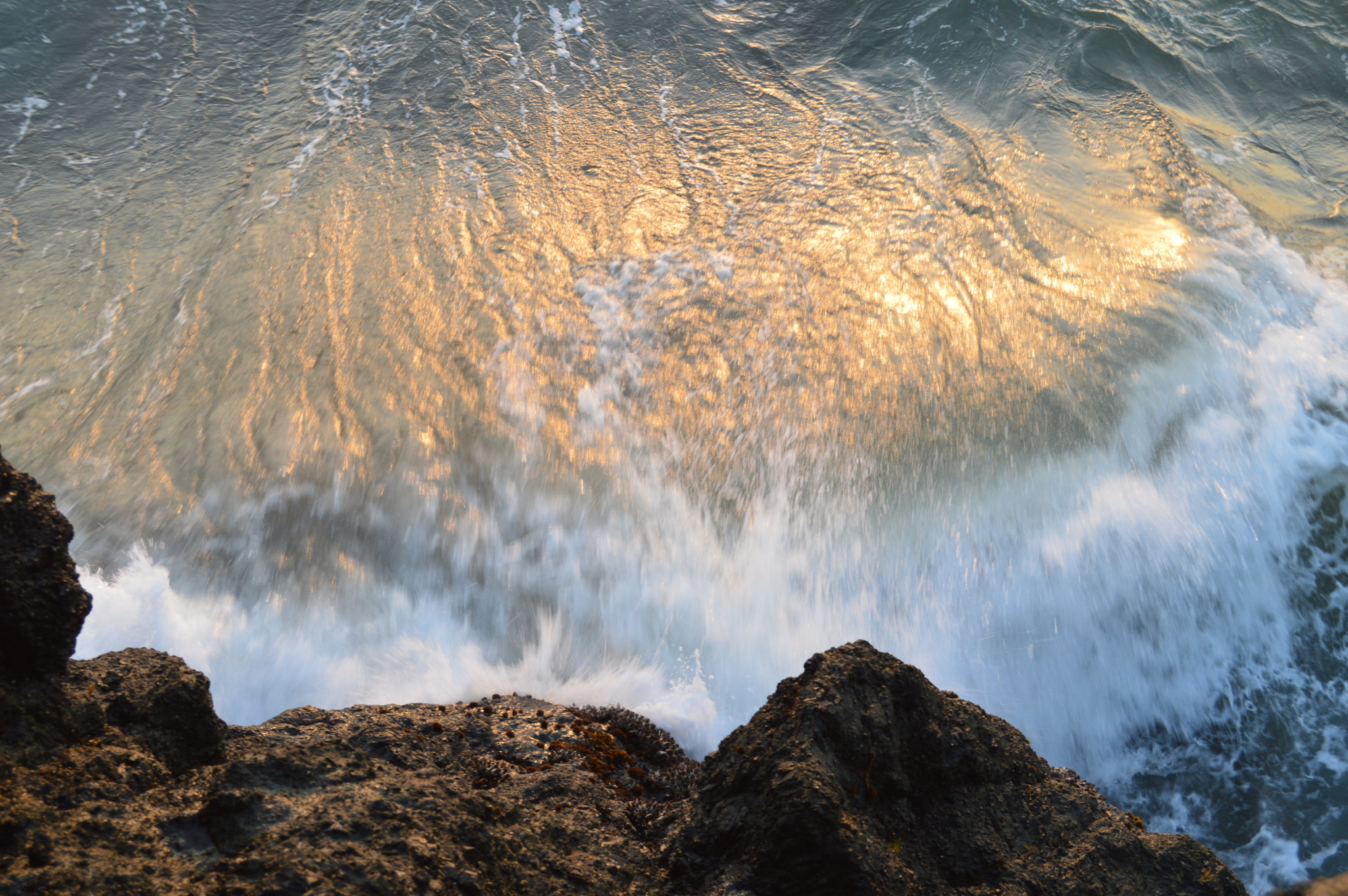 Ocean water with sunlight shining onto it crashing into rocky shore