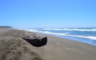 Large boulder sitting on sandy beach on clear day.