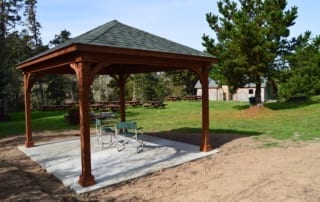 Small park shelter with two chairs under it and picnic tables in background